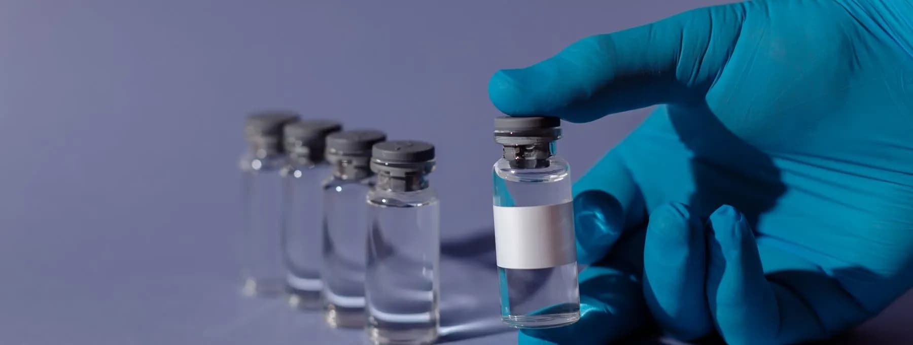 a gloved hand holding small glass vials